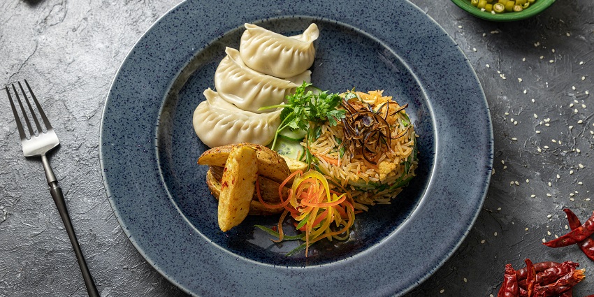 Blue plate with dumplings, fried rice, potato wedges, and fresh vegetable garnish.
