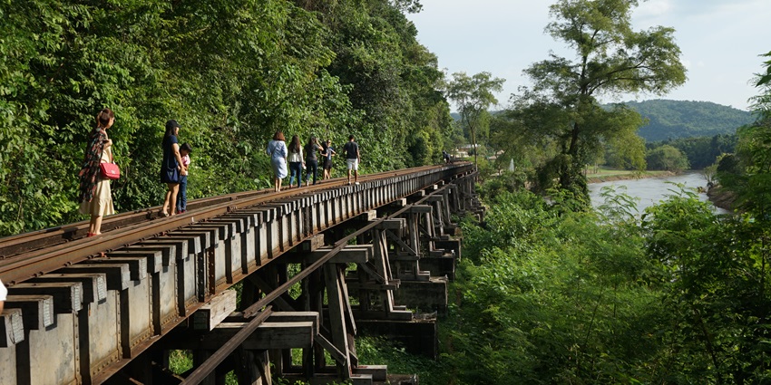 A group of visitors walks along a railway track in Erawan National Park, trekking in Thailand.