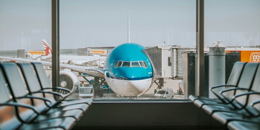 Airplane parked on runway seen through window with airport seating in foreground.

