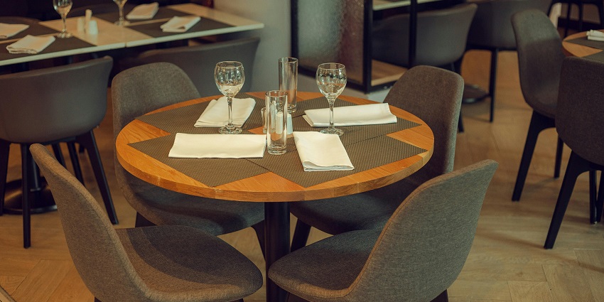 Round wooden table set with napkins and glassware in a modern restaurant dining area.