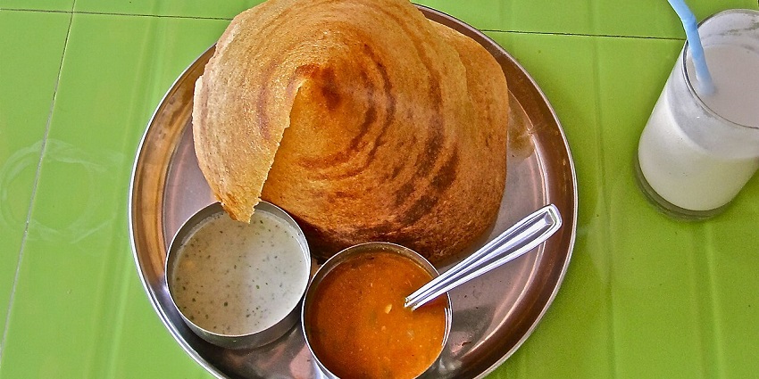 A masala dosa is served in a conical shape with chutney, sambhar and a white drink.