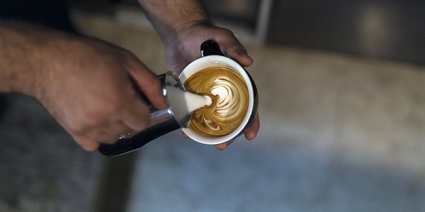 Barista pouring steamed milk into an espresso, creating smooth latte art in a black cup, one of the best cafes in Kalimpong.
