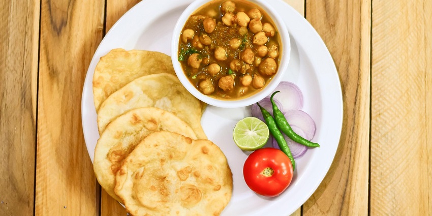 Chole bhature served on a plate at Flavours Of Punjab restaurant with side accompaniments.