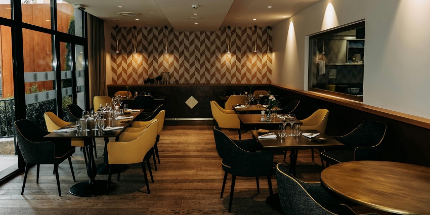 Modern restaurant with patterned walls, warm lighting, and yellow chairs around set tables, one of the restaurants in Namchi.