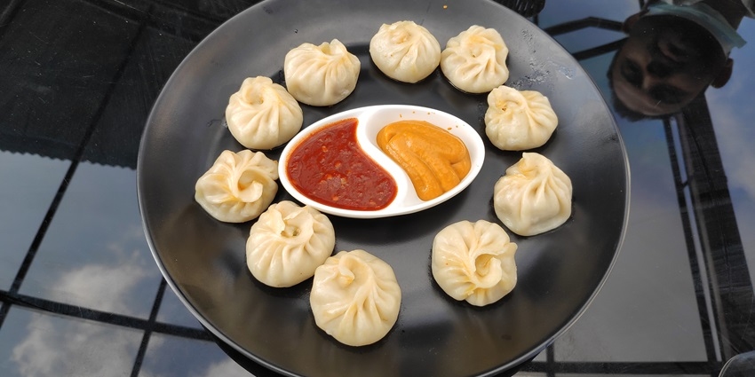A plate of hot, freshly steamed momos dumplings with two savoury dipping sauces.