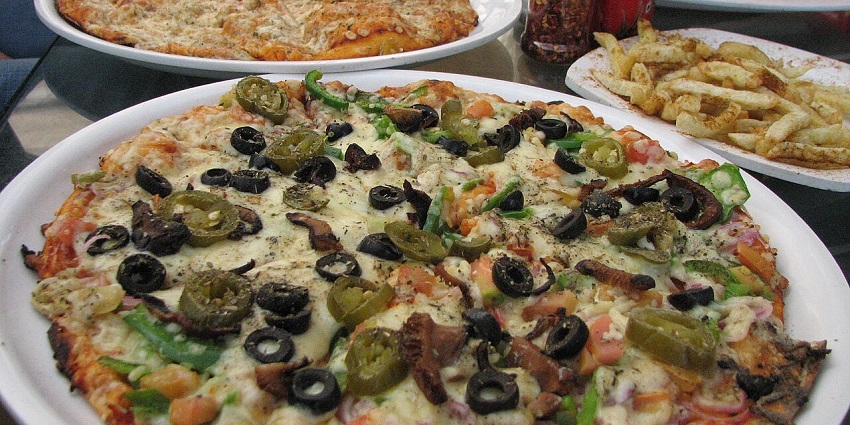 Plates of cheesy pizzas topped with olives, cheese, jalapenos, and fries served on the side.
