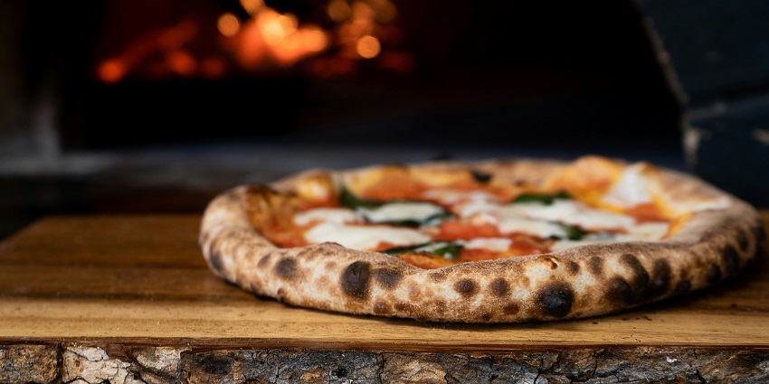 Wood-fired pizza served hot with toppings at Foxtrot restaurant on a wooden platter.
