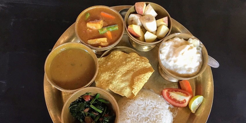 Nepali platter with rice, lentil soup, and mixed vegetable curry served in a metal tray.