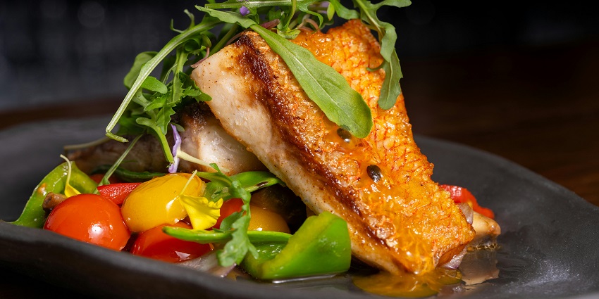 A grilled fish is served with veggies on a black plate at Full Moon Café, one of the famous restaurants in Andaman.