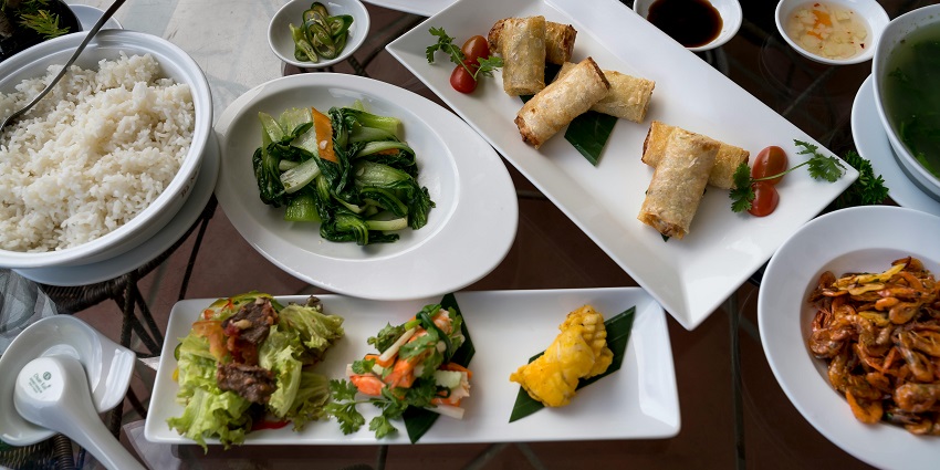 Table with rice, spring rolls, sautéed greens, and assorted Asian dishes served in bowls among the multiple restaurants in Havelock Island.
