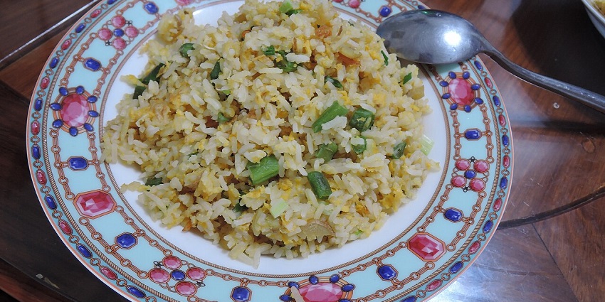 A homemade plate of fried rice with veggies like chopped beans is served at a table at one of the pure veg restaurants in Neil Island.
