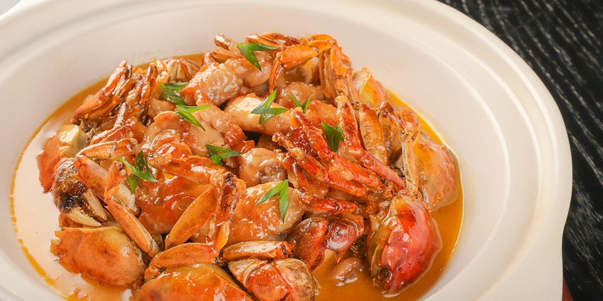 A white bowl is filled with a stew made of crab legs and a brown sauce, garnished with herbs.
