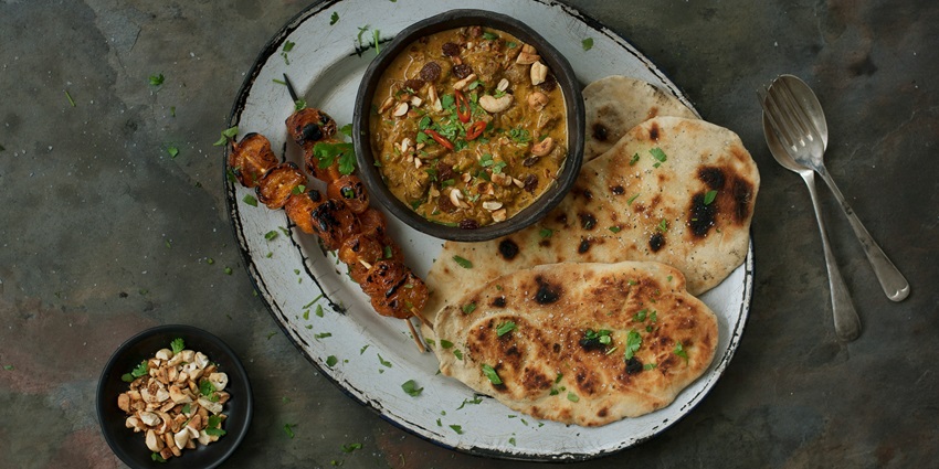 Traditional thali meal with curry, naan, and assorted side dishes served on a platter.