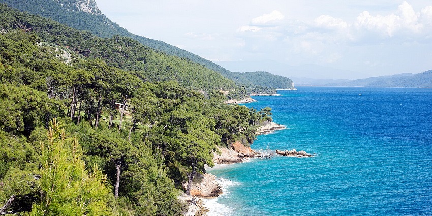 A tranquil view of Gökova Bay with calm blue waters surrounded by distant hills and coastline.
