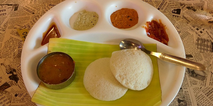 A plate of Indian food with two idlis, a bowl of sambar, and three different chutneys in one of the vegetarian restaurants in Singapore Little India.

