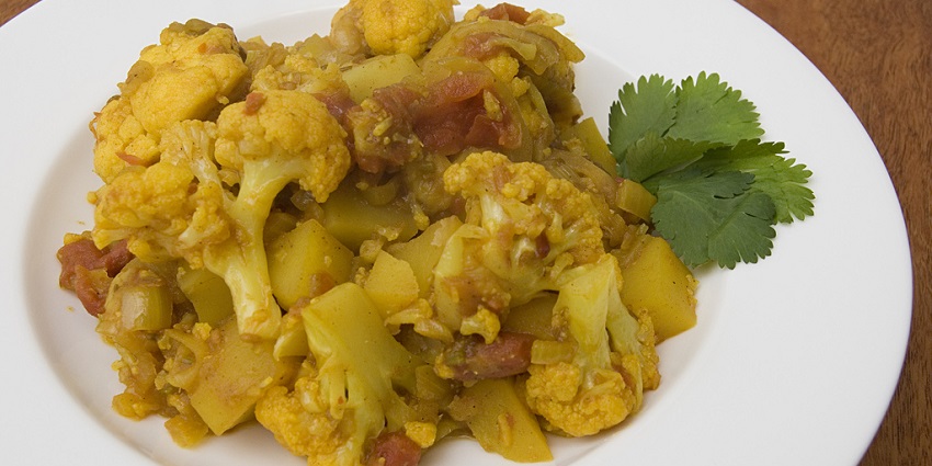 A plate of aloo gobi sabji is served with coriander leaves on a table at a restaurant.