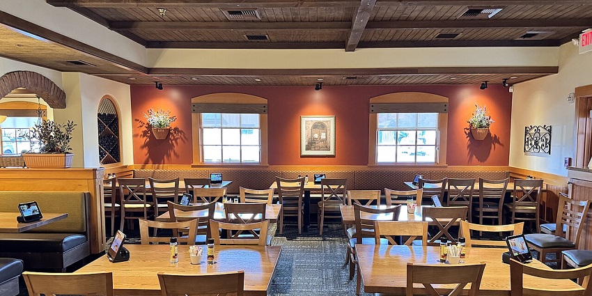 A well-lit restaurant dining room with many wooden tables and chairs, and booths.
