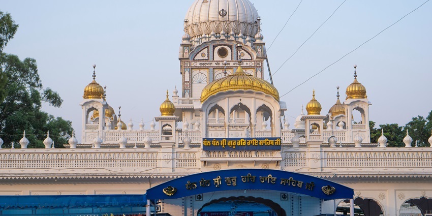 A peaceful gurudwara surrounded by greenery under a clear sky.