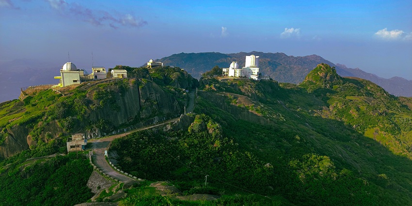A small white observatory building sits on a rocky hill with a road leading up to it.