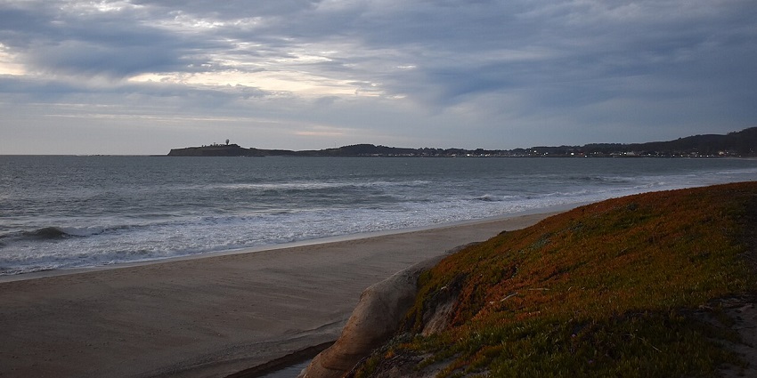 A coastal landscape with a lighthouse and gentle waves on sand, ideal for scuba diving in Karnataka.
