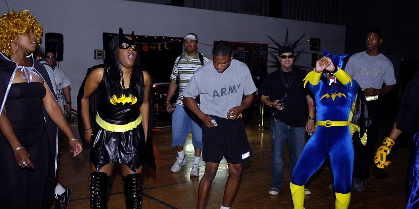 People wearing shiny superhero costumes and other costumes dance during a Halloween party.