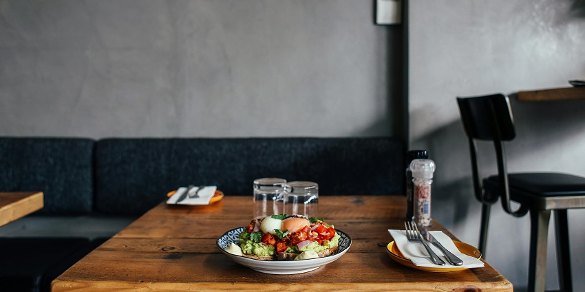 Wooden table with avocado toast, poached egg, tomato topping, and glasses of water.
