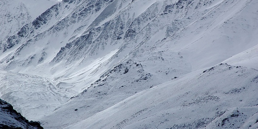 Steep snowy mountain slopes with deep ravines under white sky in national parks in Ladakh.
