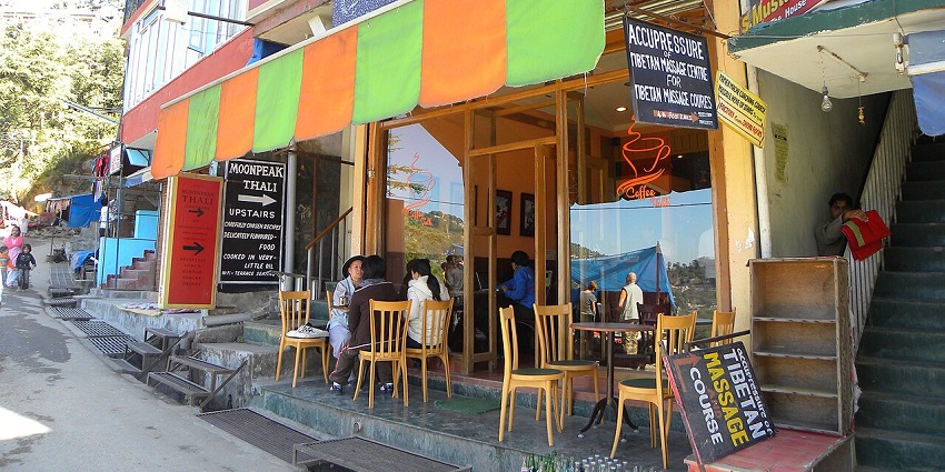 Outdoor café seating with red umbrellas and metal chairs, lively street scene in the background
