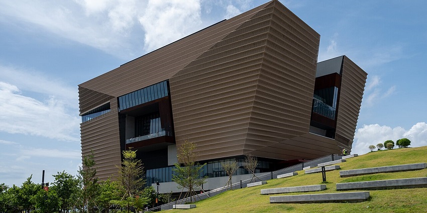 Hong Kong Palace Museum is a modern building with an angular design and a green lawn.
