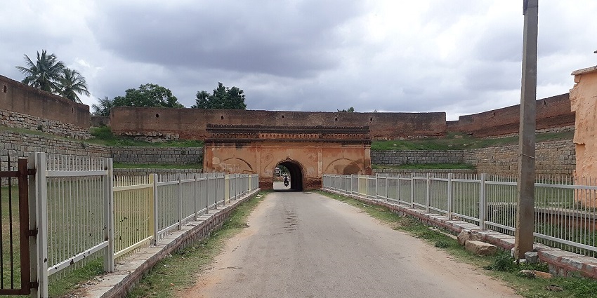 A wide shot of an ancient red stone fort with a road leading to a central archway, one of the top haunted places in Karnataka.