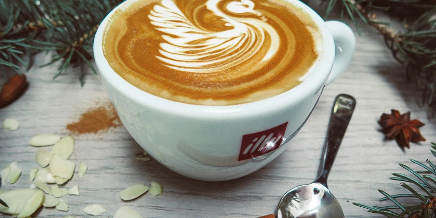 A cup of cappuccino with swan cream design served on a wooden table at Icy Spicy Cafe.