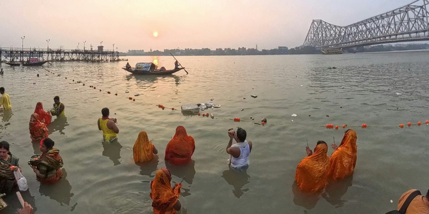 A group of women stands in water, offering prayers to the Sun God during Chhath Puja rituals.