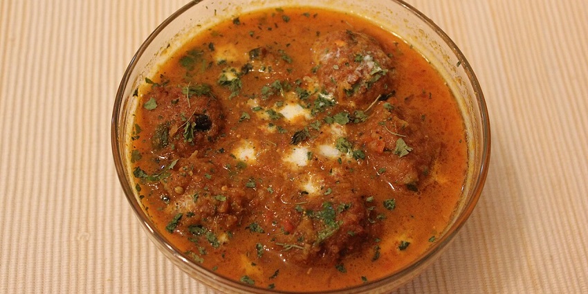 Bowl of rich curry with koftas, garnished with cream, fresh green herbs, and spicesin one of the restaurants in City Centre Siliguri.
