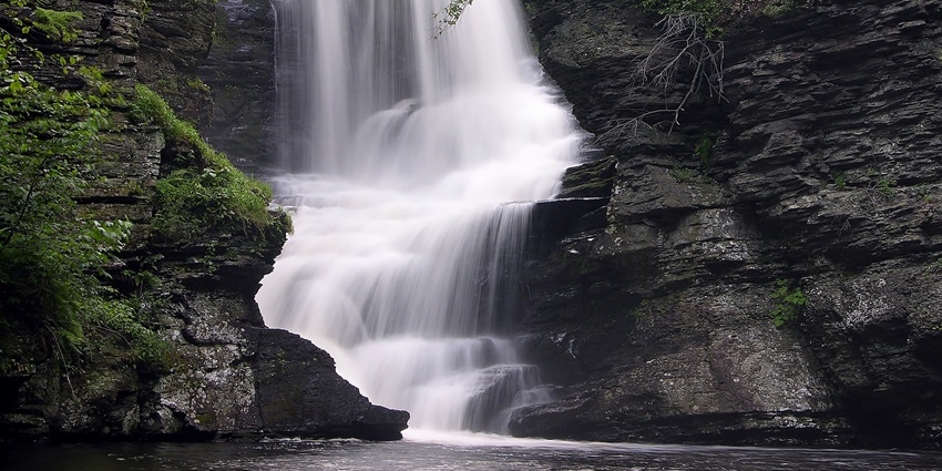A waterfall cascading down rocky cliffs with moss and greenery on the sides, one of the top waterfalls in Darjeeling.