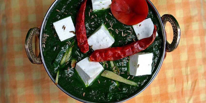 A top-down view of a bowl of palak paneer with blocks of white cheese and red peppers.
