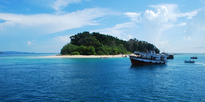 A large boat floats on a vast blue ocean near a small tropical island with a sandy beach.