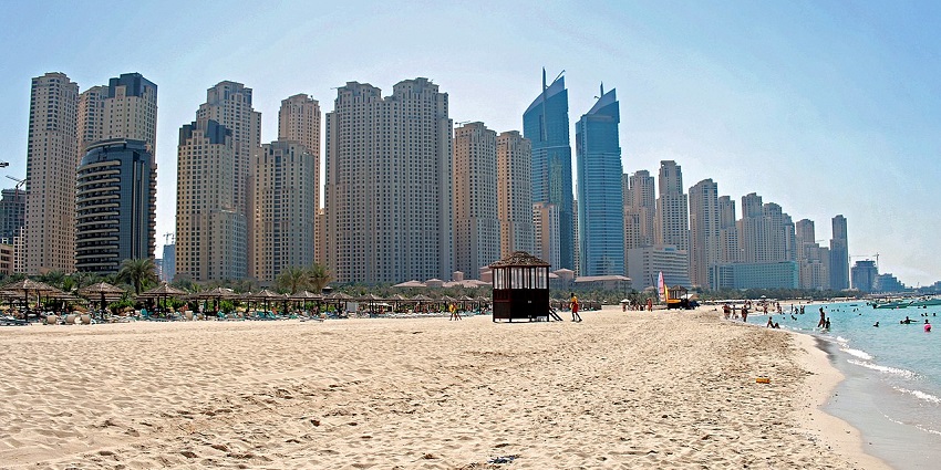 People enjoying the beach with sunbeds and umbrellas along a sandy shoreline by blue water
