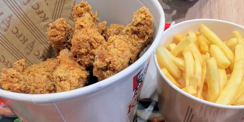 A giant bucket of crispy fried chicken pieces next to a bucket of golden french fries.
