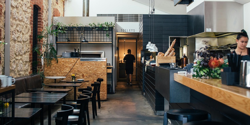 Rustic café interior with stone wall, black tables, open kitchen, one of the restaurants in Guwahati.
