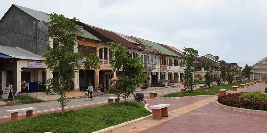 A street view in the city of Kampot, Cambodia, showing a mix of colonial-era and modern buildings.