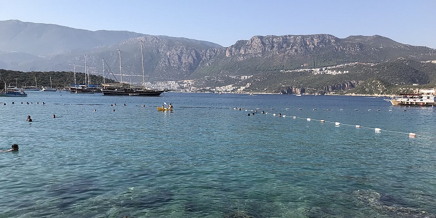 A blue clear water bay with boats, bordered by mountains and rocky shores, for scuba diving in Turkey.
