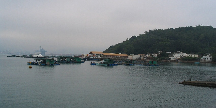 Kat O Island with floating structures on water and green cliffs under clouds in islands in Hong Kong.