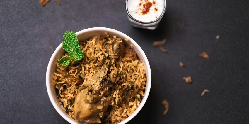 Chicken biryani served with raita at Khan Uncle's Biryani House on a white plate.
