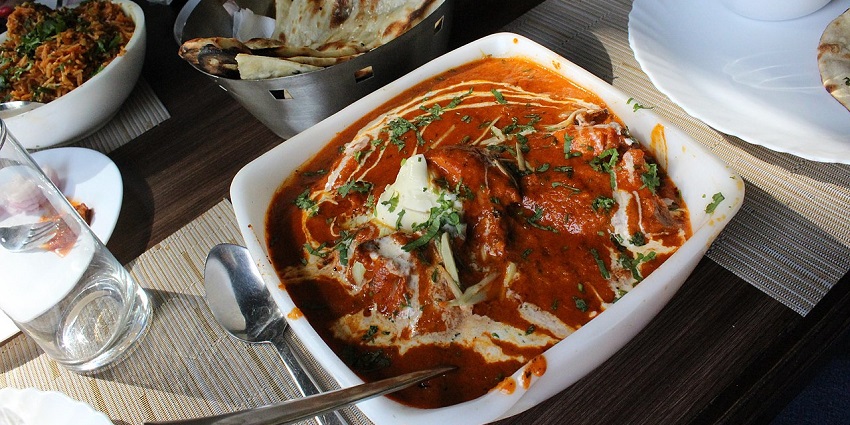A close-up shot of a rich, creamy butter chicken dish served in a bowl with naan bread, in one of the Indian restaurants in Kuala Lumpur.
