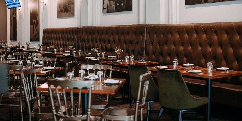 Elegant restaurant with long tufted leather seating, wooden tables, and framed wall art.