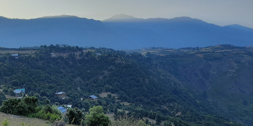 The sun's rays peek over a mountain ridge, lighting up a green, hilly landscape.
