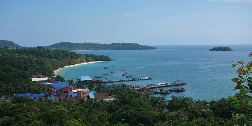 A photograph of a pristine, white-sand beach with turquoise water and leaning palm trees on the island.