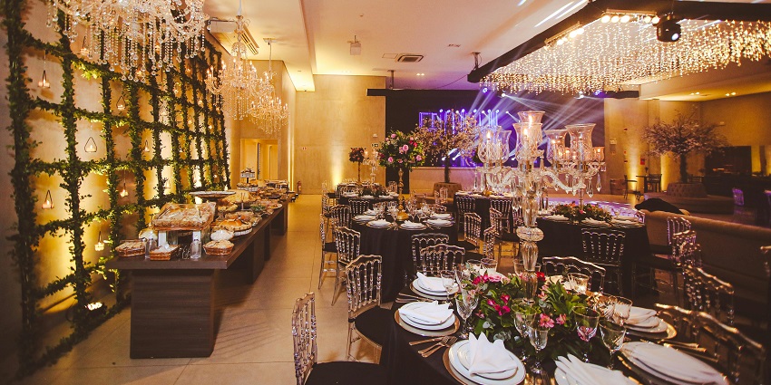 Elegant banquet hall with chandeliers, floral décor, buffet setup, and round dining tables.
