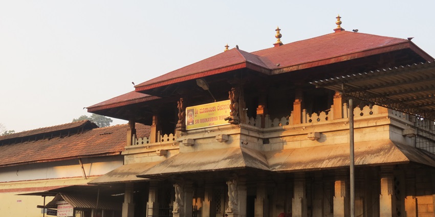 A temple building with a red-tiled roof and multiple stone pillars stands in a plaza.