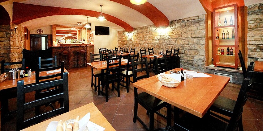 A restaurant with a stone wall and arched ceiling, with many wooden tables and chairs, one of the best Indian restaurants in Singapore, Little India.
